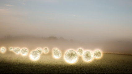 Surreal, mysterious photo collage of glowing moons hover over a foggy farmer's field.