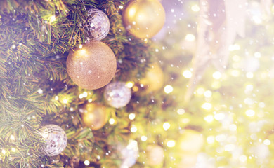 Gold bauble hanging from a decorated Christmas tree with bokeh and snow, copy space. Xmas holiday background.
