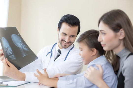 Portrait of smiling handsome doctor working in hospital. Doctor showing x-ray film to boy with happy emotion.