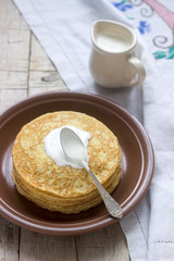 Stack of Russian pancakes with sour cream - blini on a plate on wooden table.