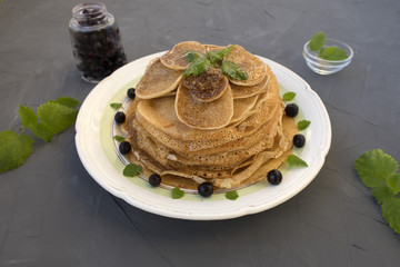 Pancakes are located in a plate on a gray background, decorated with berries and mint leaves.