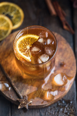 Cocktail with iced tea, whiskey, orange and ice in a glass on the wooden tray on the dark background