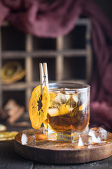 Cocktail with iced tea, whiskey, orange and ice in a glass on the wooden tray on the dark background