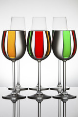 Wineglasses on a shiny surface with different colour fluids that distort reflection