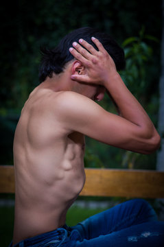 Side view of shirtless man suffering from anorexy, screaming with both arms around her head suffering pain, in a blurred background