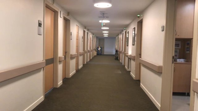 Walk through long, empty medical center building corridor