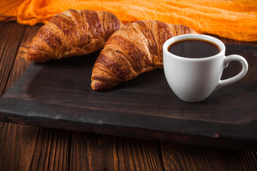 Freshly baked croissant jam, cup of coffee in white cup on brown wooden background. French breakfast. Fresh pastries for breakfast. Modern dark mood style. Delicious dessert. Horizontal banner