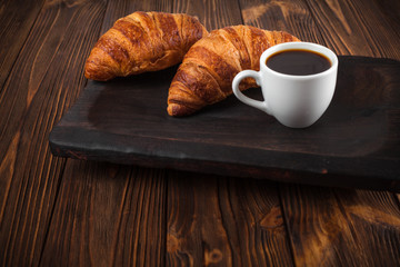 Freshly baked croissant jam, cup of coffee in white cup on brown wooden background. French breakfast. Fresh pastries for breakfast. Modern dark mood style. Delicious dessert. Horizontal banner
