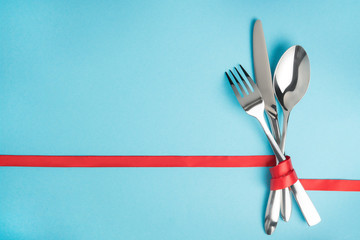 Fork, spoon and knife tied with a red ribbon on blue background