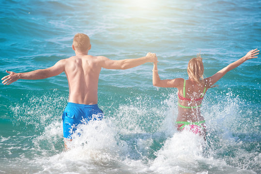 Caucasian couple running into the sea water. Back view.