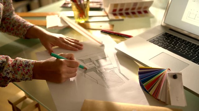 view from above, on the hands of an architect drawing a kitchen plan by hand. On his desktop a laptop, color chart and drawing tools