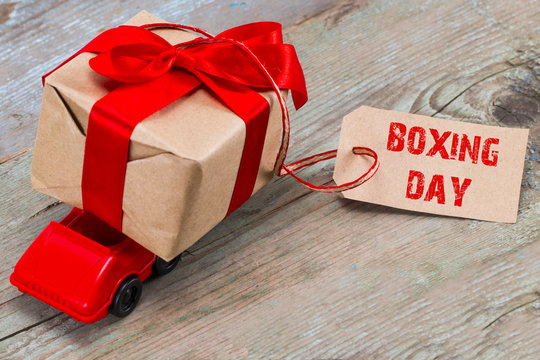 The BOXING DAY concept. Red toy car delivering gifts box with tag with text: BOXING DAY on wooden background