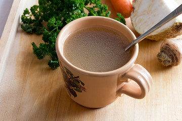 Chicken stock in a vintage mug with a spoon and vegetables
