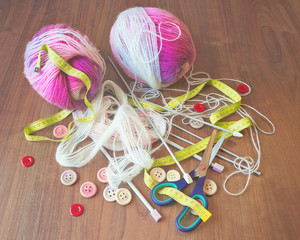 Skeins of thread, buttons, measuring tape and scissors on wooden background.