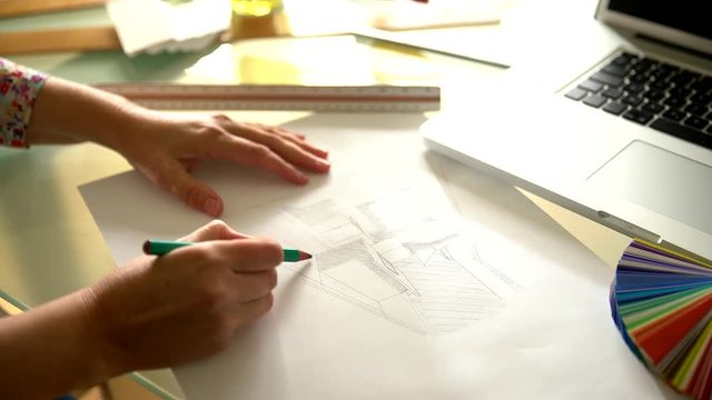view from above, on the hands of an architect drawing a kitchen plan by hand. On his desktop a laptop, color chart and drawing tools