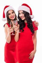 Portrait of two happy smiling girls in red dresses holding glasses with champagne while toasting and looking at camera isolated over white background