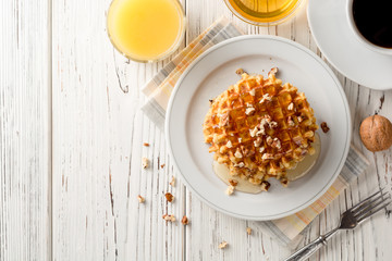 Belgian waffles with honey and walnuts on white wooden background.