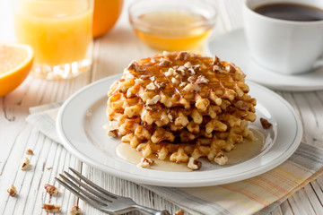 Belgian waffles with honey and walnuts on white wooden background.