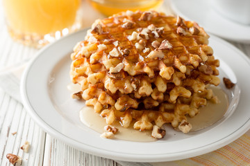 Belgian waffles with honey and walnuts on white wooden background.