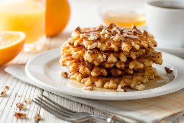 Belgian waffles with honey and walnuts on white wooden background.