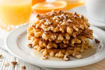 Belgian waffles with honey and walnuts on white wooden background.