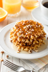 Belgian waffles with honey and walnuts on white wooden background.