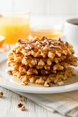 Belgian waffles with honey and walnuts on white wooden background.