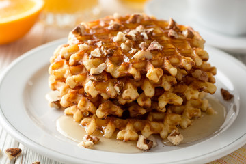Belgian waffles with honey and walnuts on white wooden background.