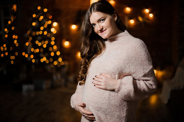 Beautiful pregnant woman with long hair dressed in sweater against the Christmas tree