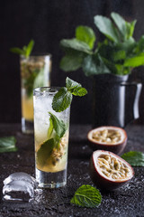 Cold mojito with passion fruit, mint and ice on the black background