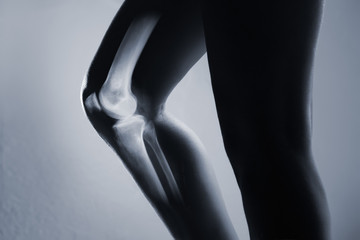 Human knee joint and leg in x-ray, on gray background. The knee joint is highlighted by red colour.