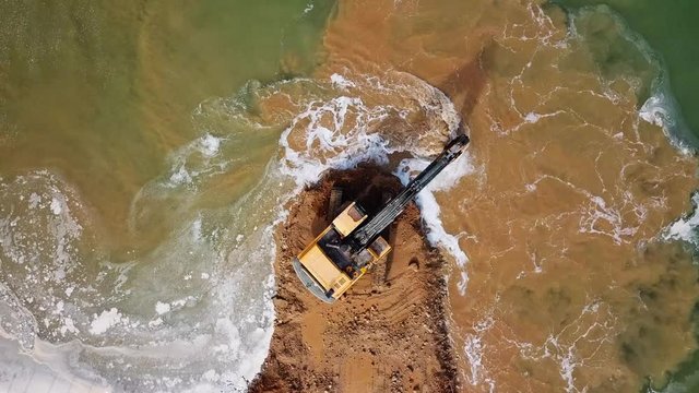 Excavator scooping and unloading soil onto a waiting large truck - Top down aerial footage