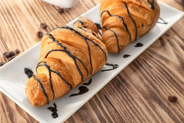Plate with tasty croissants on wooden table, closeup