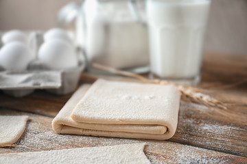 Raw flaky dough on wooden table, closeup