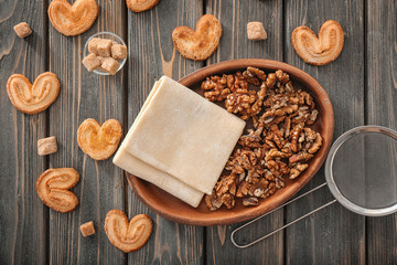 Bowl with raw flaky dough and walnuts on wooden background, top view
