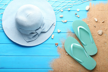Beach hat with pebble and flip flops on wooden table
