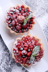 Dessert tartlet with berries and powdered sugar on grey wooden table