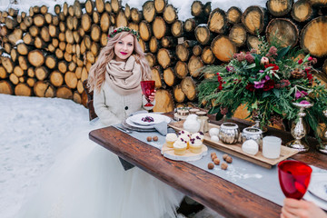 Young bride is holding a wine glass, sitting on the decorated table. Selective focus on the girl. Winter wedding
