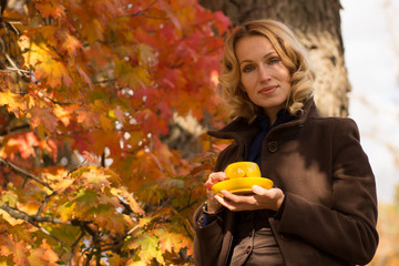 Pretty woman is holding cap under an autumn tree