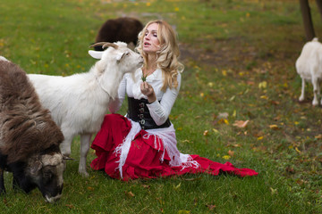 Happy woman stroking goats on a green glade