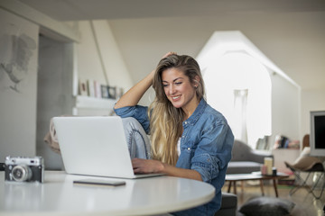 Young beautiful woman works for a computer from a home with a laptop on a white desk as a freelancer