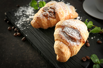 Wooden board with tasty croissants on table, closeup