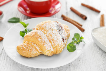 Plate with tasty croissant on white wooden table