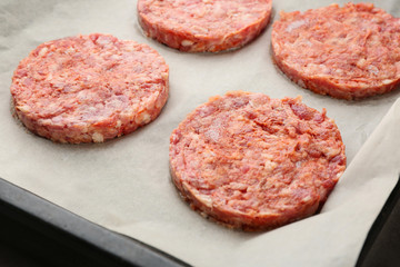 Baking sheet with raw burger patties, closeup