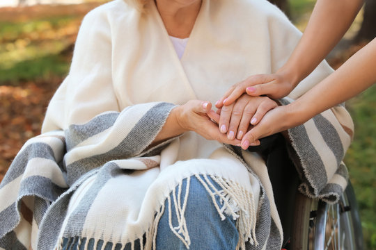Senior woman and young caregiver holding hands outdoors, closeup