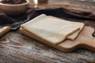 Wooden board with raw flaky dough on table