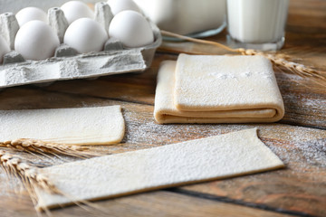 Raw flaky dough and egg carton on wooden table