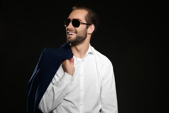 Young handsome man in sunglasses smiling on black background