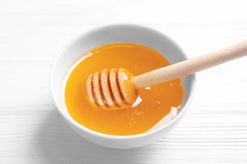 Bowl with honey and dipper on white wooden background
