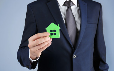 Real estate agent holding house model on grey background